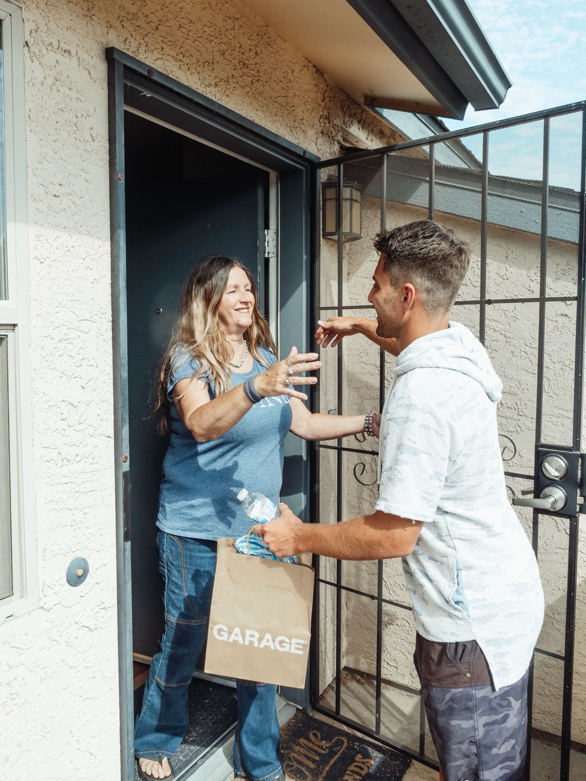 A neighbour greets somebody at her door, a bag in hand.